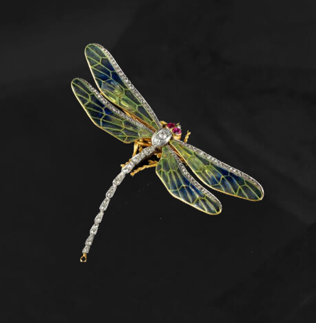 Une broche libellule ornée de pierres précieuses, avec des ailes et une queue incrustées de diamants, des détails en émail bleu et jaune et des yeux en rubis.