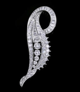 Broche argentée en forme de feuille, incrustée de multiples pierres transparentes rondes et taillées en baguette sur fond noir.