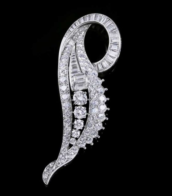 Une broche en argent en forme de feuille allongée et tourbillonnante, densément sertie de nombreux diamants ronds et taille baguette.