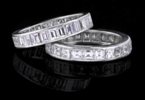 Deux alliances en argent serties de diamants rectangulaires taille émeraude, se détachant sur un fond noir réfléchissant.