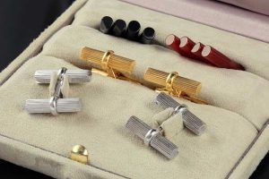 Un coffret à bijoux doublé de crème contenant deux boutons de manchette argentés et deux dorés, ainsi que des jeux de clous d'oreilles noirs et rouges.