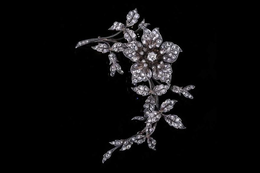 Broche florale incrustée de diamants, ornée d'une fleur proéminente à cinq pétales et de feuilles retombantes sur fond noir.