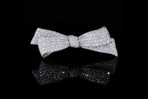 Une broche en forme de nœud incrustée de diamants, centrée sur un fond noir avec un reflet en dessous.