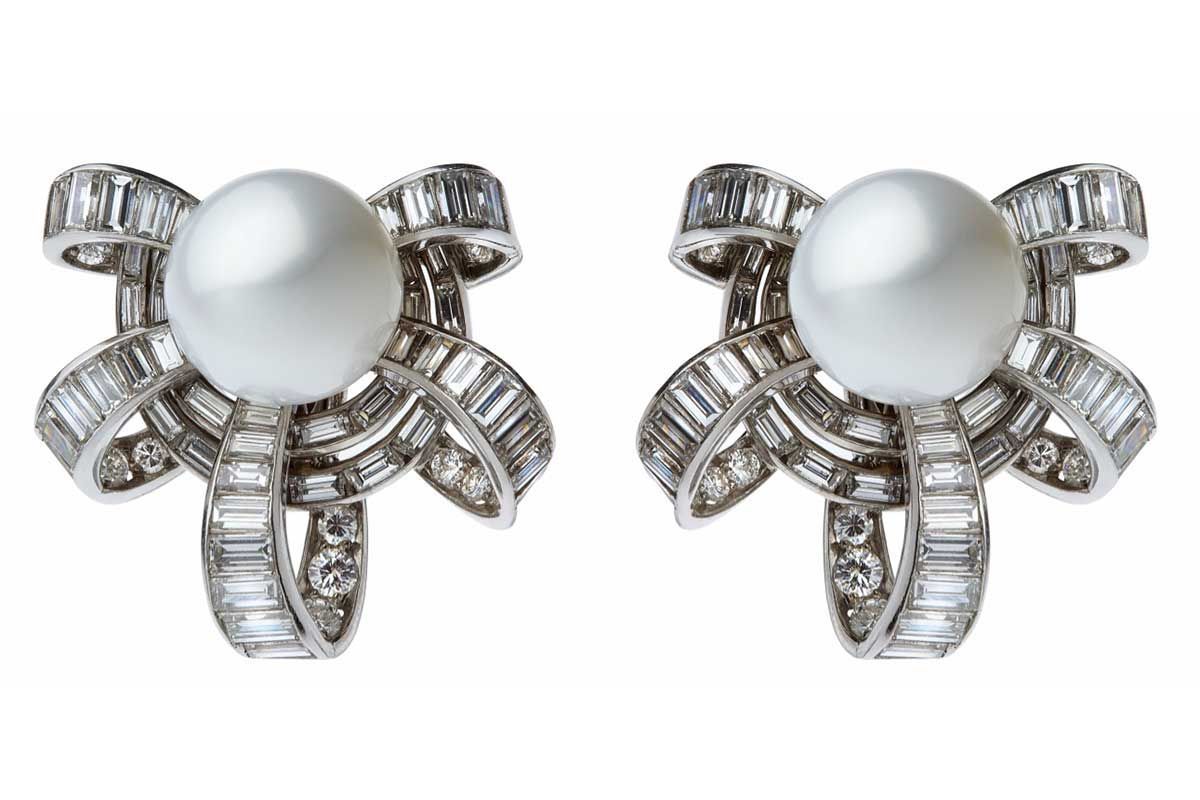 Une paire de boucles d'oreilles élégantes ornées de perles blanches centrales encadrées de motifs complexes en forme de nœud, sertis de diamants baguette.