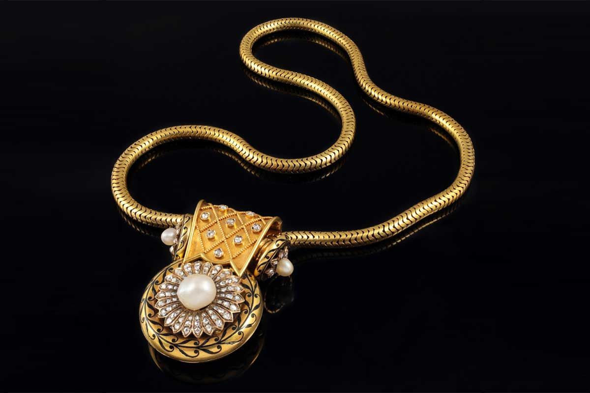 Un collier en or avec une chaîne texturée et un pendentif rond orné d'une perle centrale, de pierres scintillantes et d'une gravure en or.