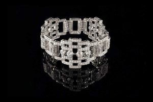 Un large bracelet articulé en platine serti de diamants selon un motif géométrique de style Art déco sur fond noir.