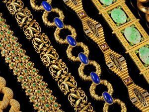 Plusieurs bracelets en or finement ouvragés, disposés en rangées sur un fond noir.
