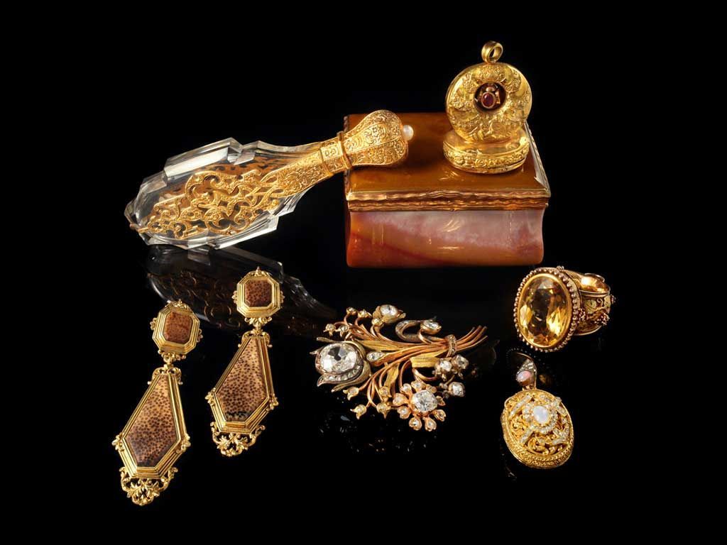 Une collection de bijoux anciens en or, un flacon de parfum en cristal orné et une petite boîte disposés sur un fond noir.