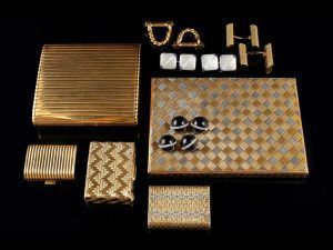 Une collection d'accessoires en or, comprenant des étuis à cigarettes, des briquets et des boutons de manchette, disposés sur un fond sombre.