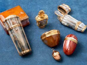 Une collection de boîtes en pierre dure et de flacons de parfum anciens aux finitions dorées, disposés sur une surface bleue.