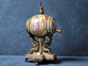 Un distributeur en porcelaine orné, en forme de tonneau, sur un support métallique orné de figures mythiques et d'illustrations classiques.