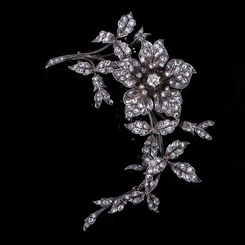 Broche florale incrustée de diamants, ornée d'une grande fleur centrale et de feuilles enroulées sur fond noir.