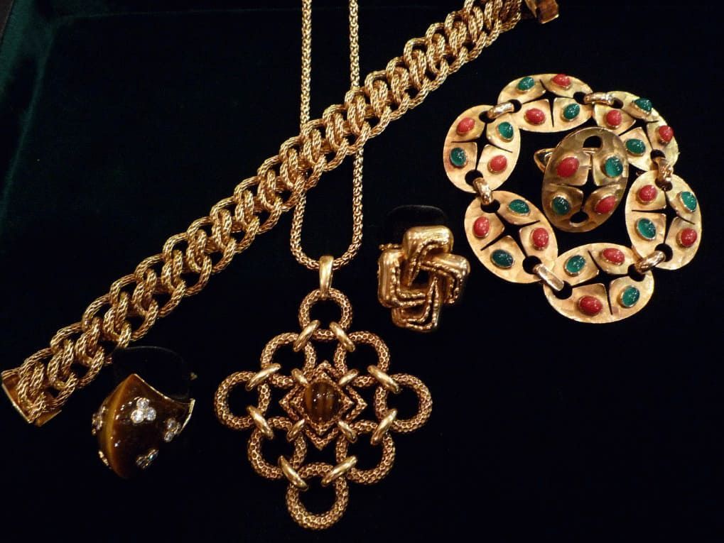 Une collection de bijoux en or, comprenant un collier à chaîne, un bracelet texturé, une bague et une broche ornée de pierres précieuses rouges et vertes.