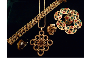 Une collection de bijoux dorés sur fond noir, comprenant un bracelet à maillons, un pendentif, deux bagues et une broche.