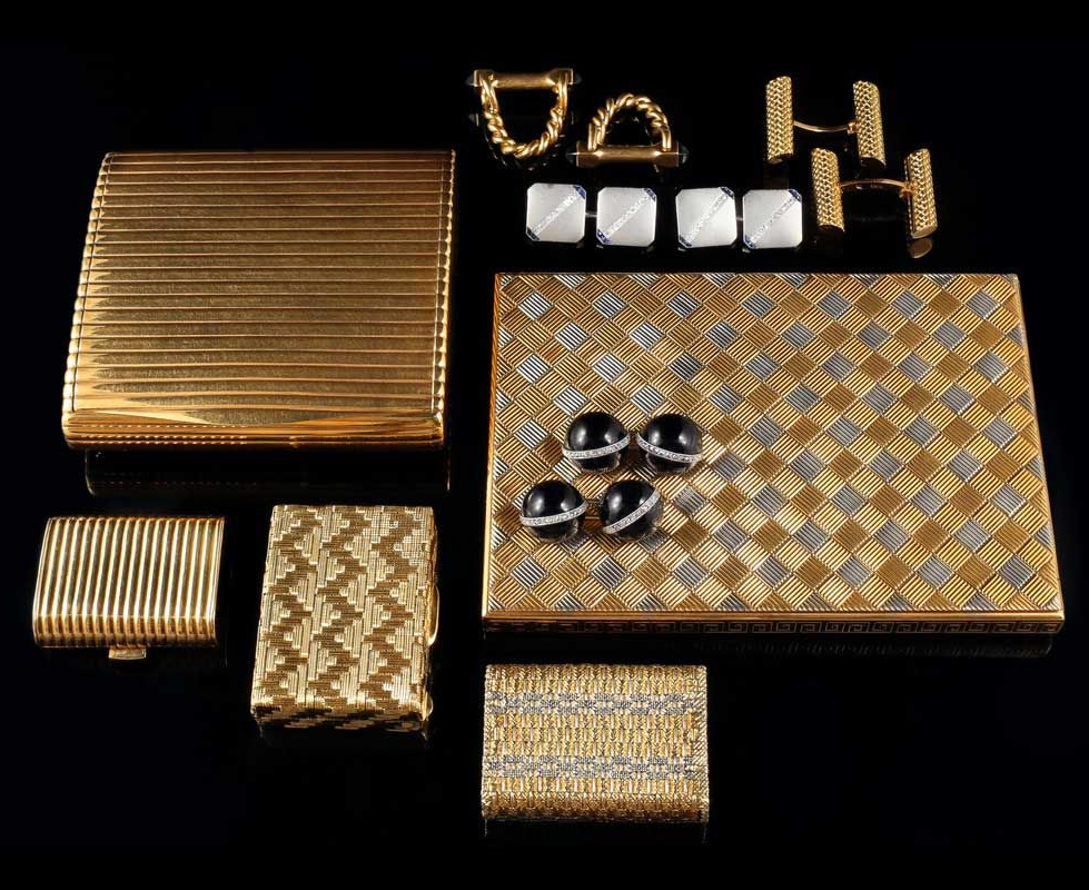 Une collection d'accessoires aux tons or et argent, comprenant des trousses de toilette, des étuis à cigarettes et des boutons de manchette, sur fond noir.