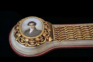Broche en or ornée d'un portrait miniature ovale représentant une personne, fixée sur un anneau en or texturé et tissé.