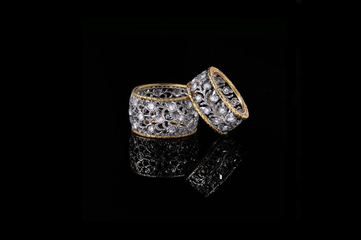 Deux bagues ornées, cerclées d'or, présentant des filigranes complexes et des pierres scintillantes incrustées sur fond noir.