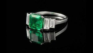 Une bague de fiançailles en platine avec une grande émeraude rectangulaire en pierre centrale, flanquée de diamants taille baguette.