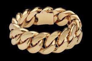 Un bracelet cubain en or massif avec fermoir sécurisé, sur fond noir uni.