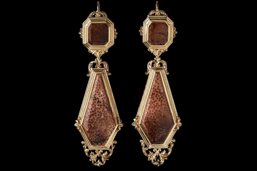 Paire de boucles d'oreilles pendantes ornées, bordées d'or, présentant des incrustations de pierres texturées brun rougeâtre sur fond noir.