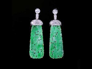 Une paire de boucles d'oreilles de style Art déco, composées de plaques de jadéite verte sculptées, suspendues à des supports en argent incrustés de diamants.