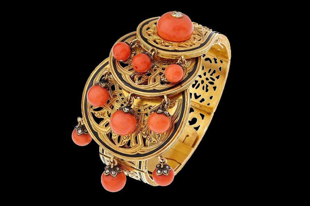 Un bracelet manchette en or orné de filigranes complexes, de disques circulaires superposés et de perles de corail pendantes sur fond noir.