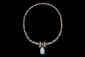Un collier en argent sur fond noir, orné d'un nœud central et d'une pierre précieuse en forme de larme bleu pâle pendante.