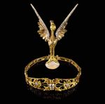 Un bracelet en or orné d'un oiseau aux ailes serties de pierres précieuses, perché sur une opale ovale, le tout sur fond noir.