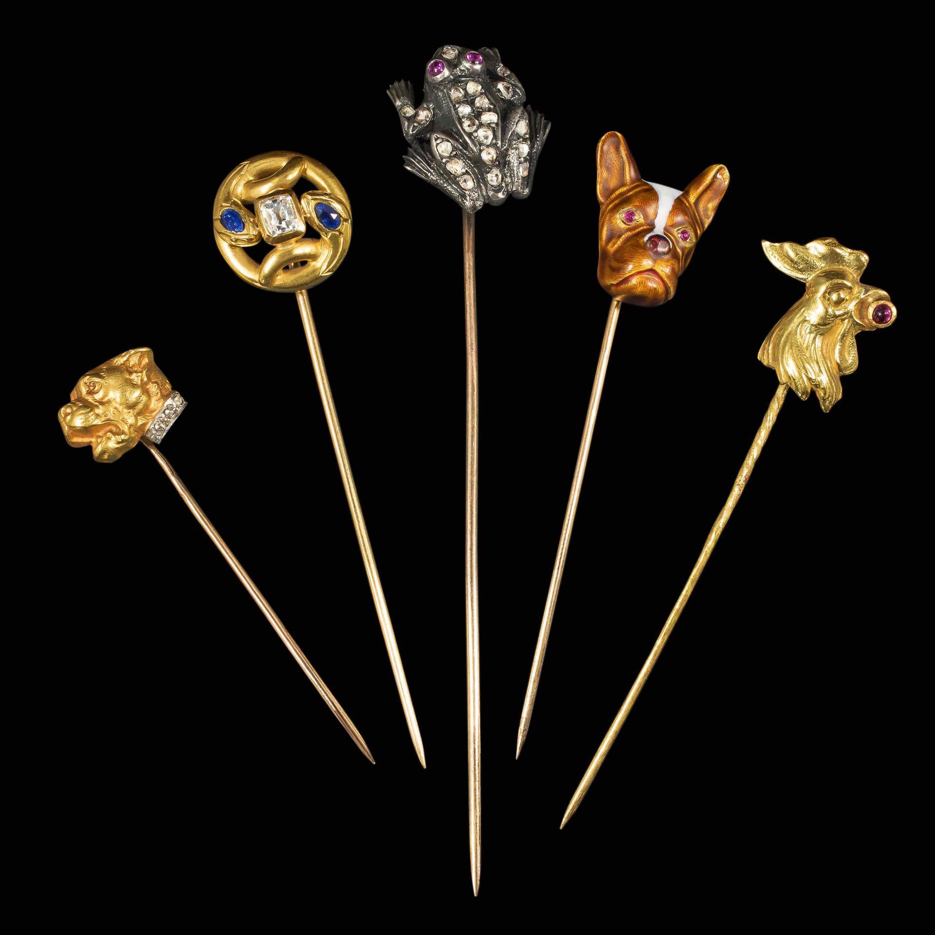 Cinq épingles à cravate anciennes ornées de motifs animaliers et décoratifs en or et pierres précieuses sur fond noir.