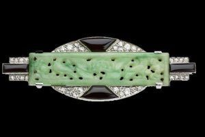 Une broche Art Déco ornée d'une barrette en jade vert sculpté, de détails en onyx noir et d'un pavage de diamants serti sur du métal blanc.