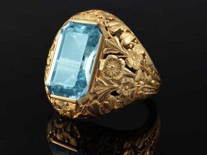 Une bague en or ornée d'une grande pierre précieuse rectangulaire bleu clair, sertie sur un fond sombre avec reflets.