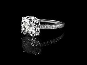 Bague de fiançailles en argent sertie de diamants, avec une pierre centrale taille coussin et des diamants latéraux sertis pavé sur fond noir.