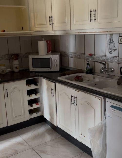 Cocina color crema con gabinetes, microondas, fregadero y salpicadero de azulejos.
