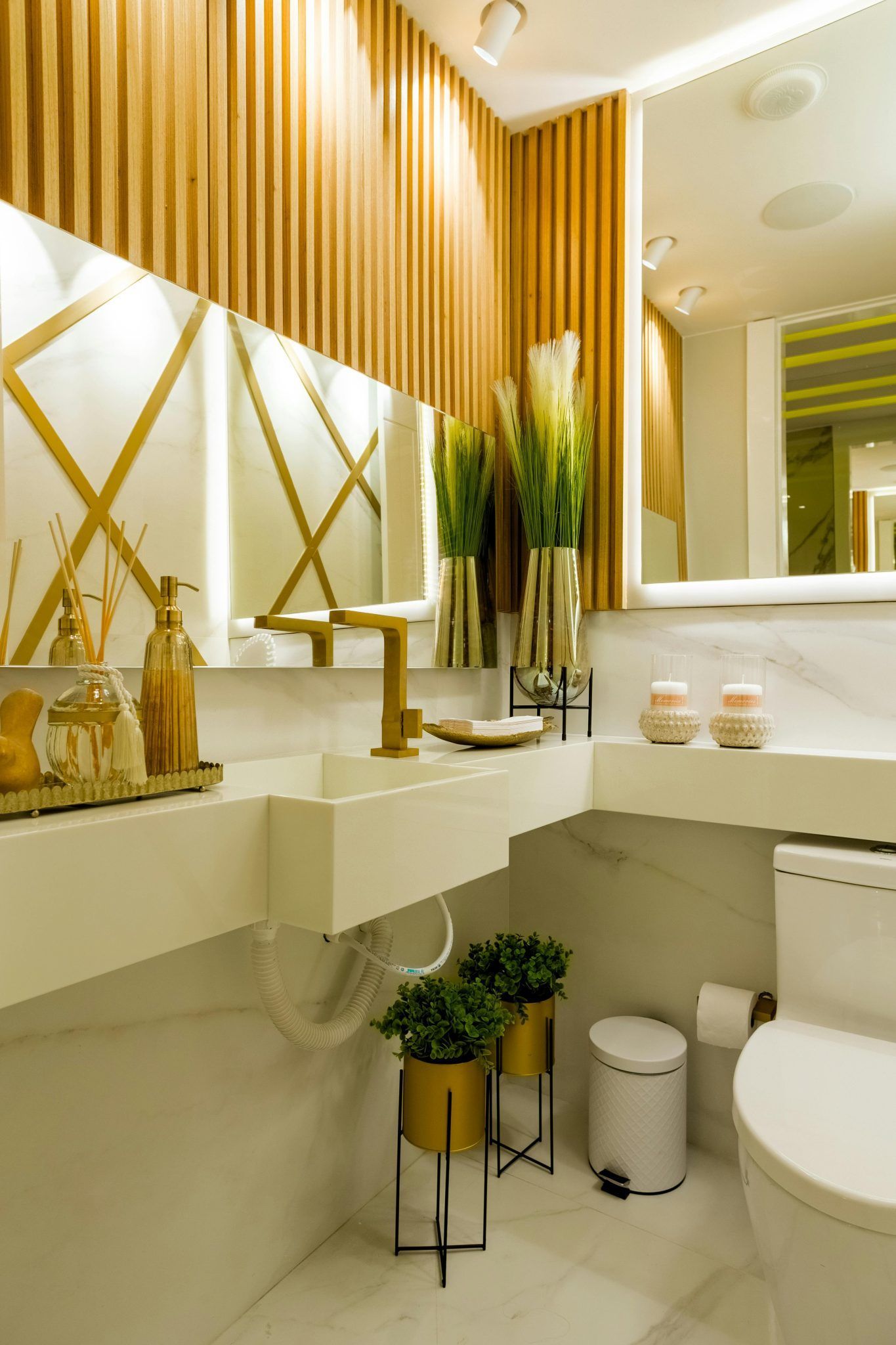 Baño moderno con paneles de madera, accesorios dorados y encimeras blancas.