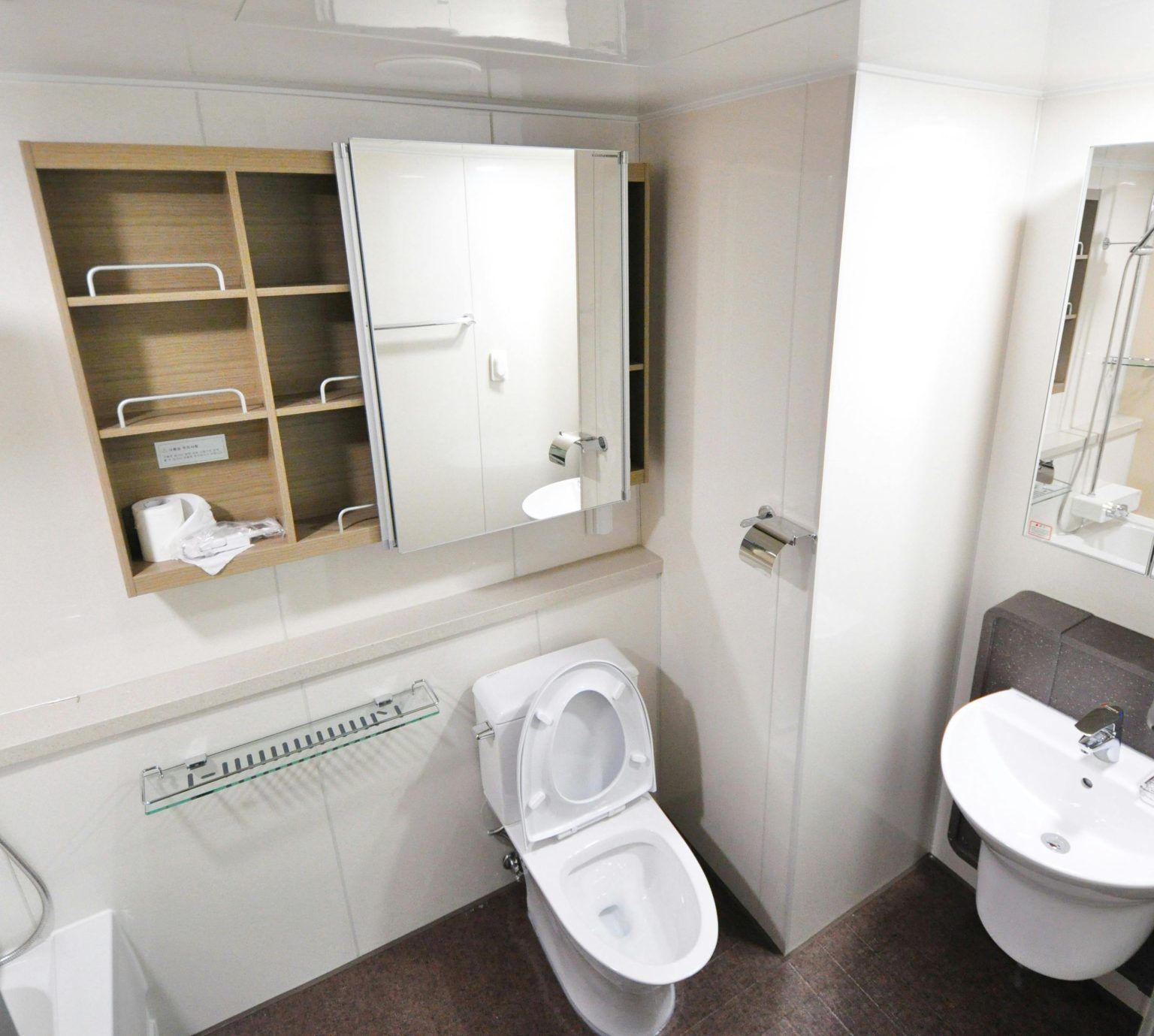 Baño pequeño con inodoro, lavabo y espejo. Paredes blancas y suelo marrón.