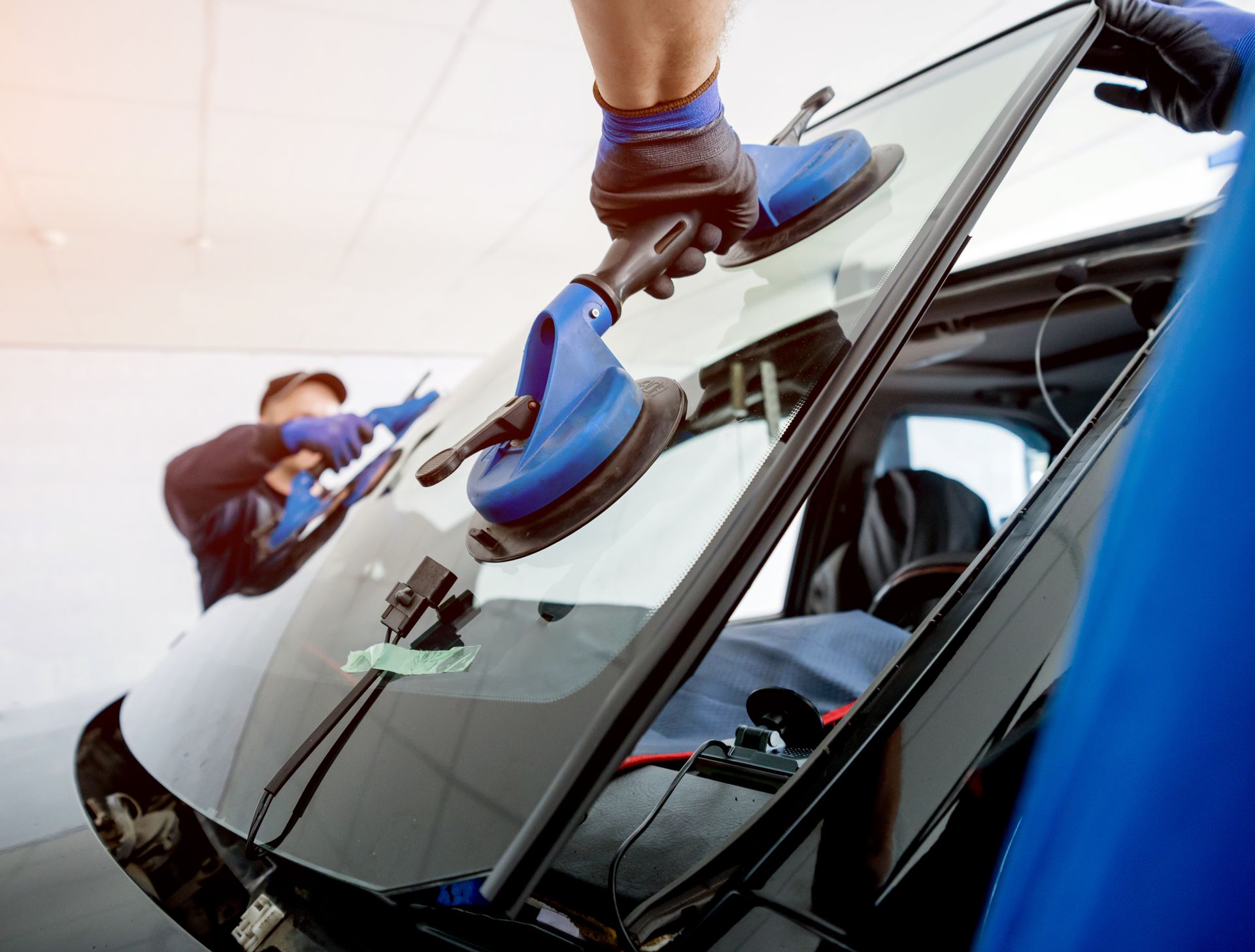 Des ouvriers, portant des gants bleus et utilisant des outils de nettoyage visibles, polissent le pare-brise d'une voiture.