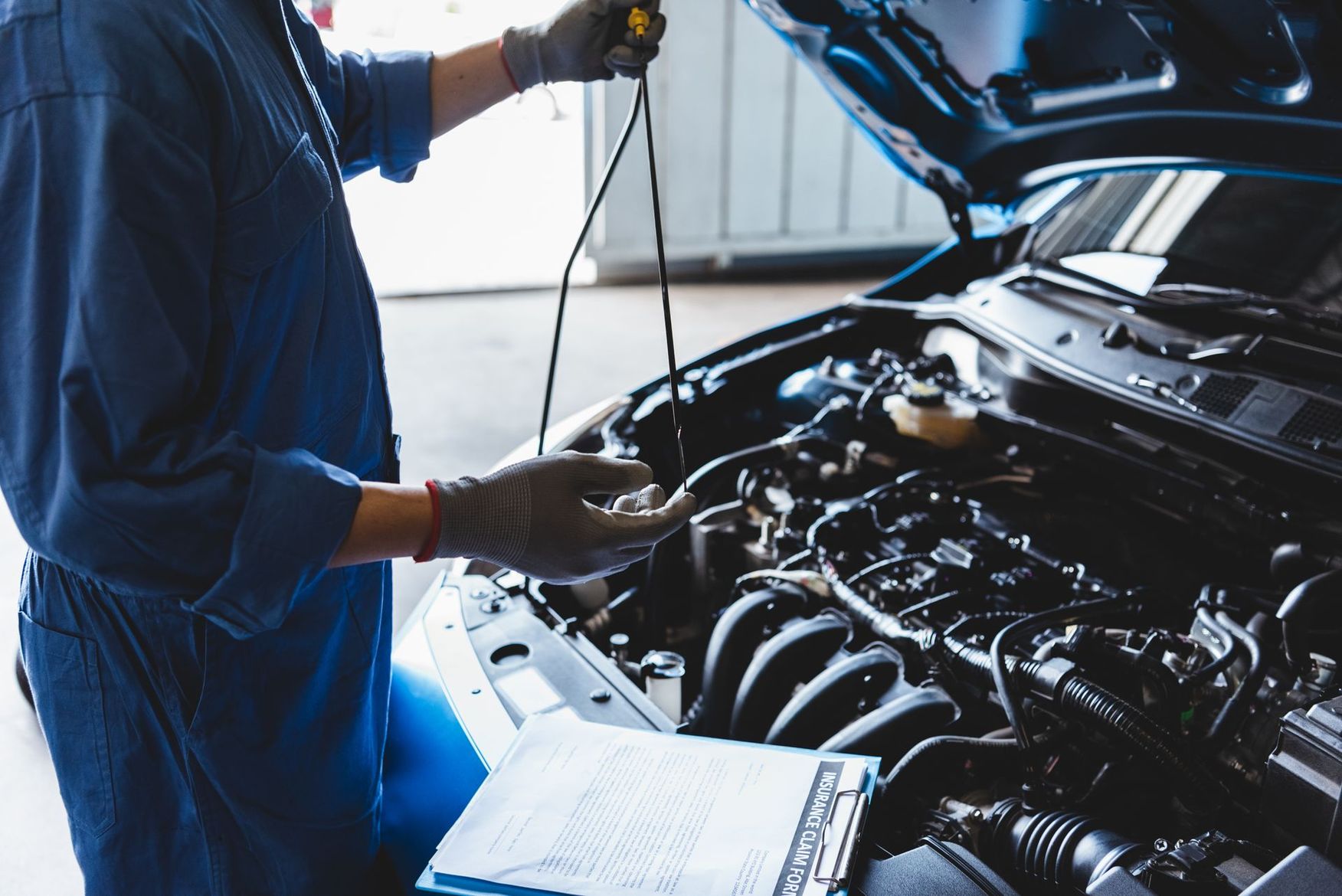 Un mécanicien inspecte le moteur d'une voiture dans un garage, vêtu d'une combinaison bleue et de gants.