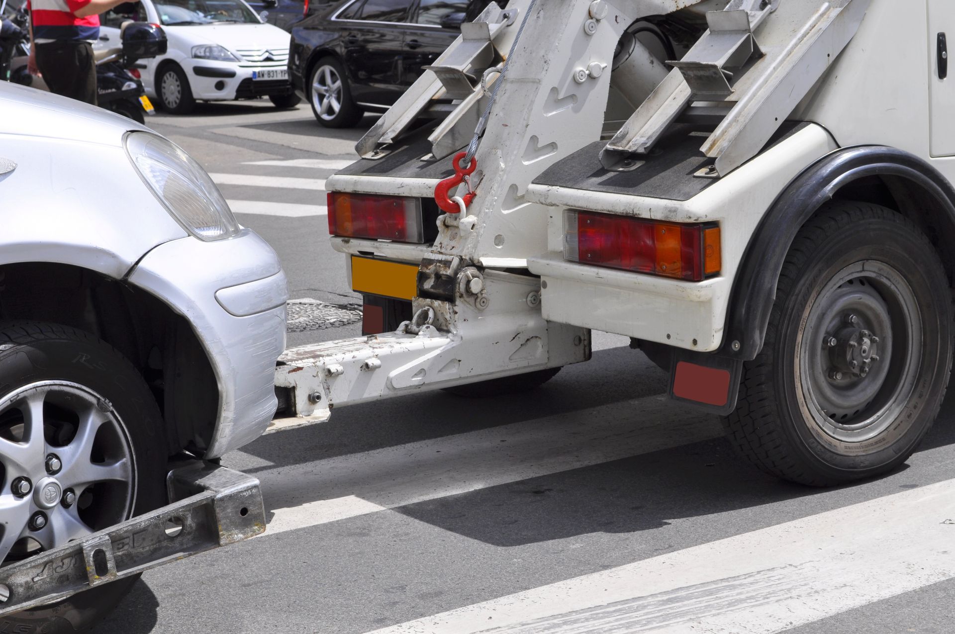 Une dépanneuse remorque une voiture grise dans une rue de la ville, près d'un passage piéton.
