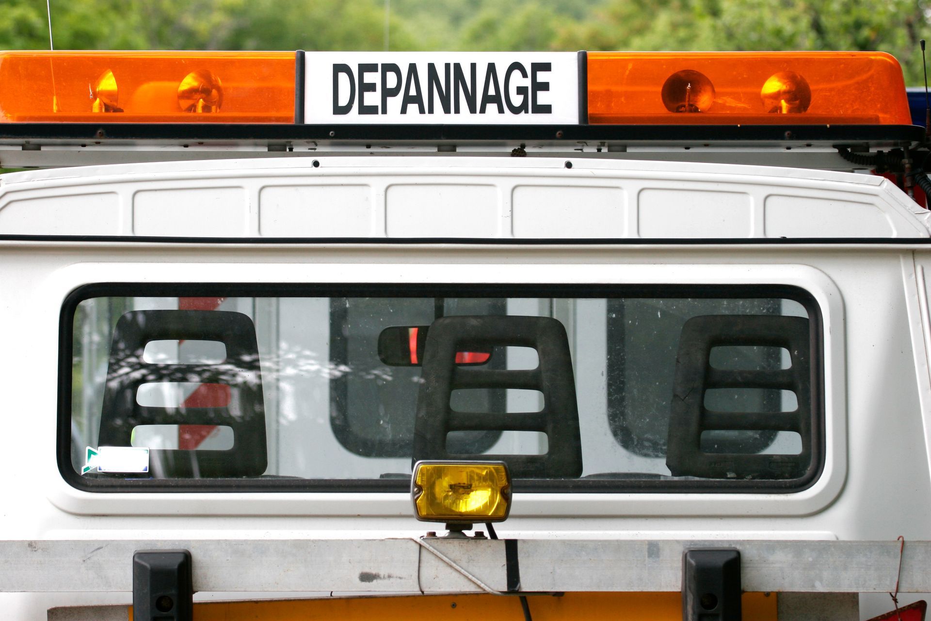 Lunette arrière d'une dépanneuse avec gyrophares orange et panneau DÉPANNAGE sur le dessus