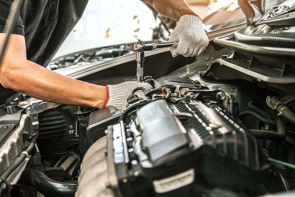 Mécanicien travaillant sous le capot ouvert d'une voiture, inspectant les composants du moteur avec des gants