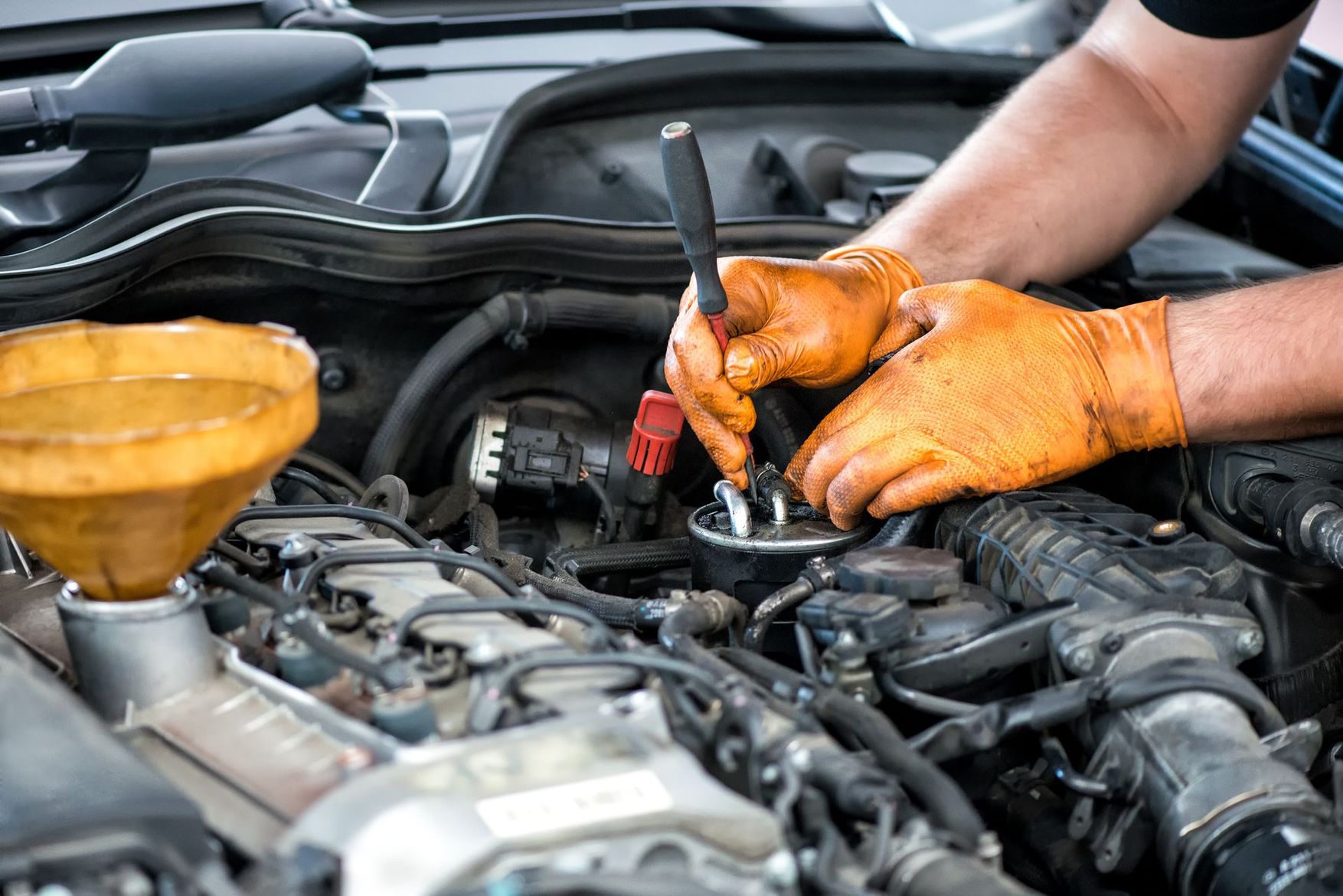 Un mécanicien portant des gants orange répare le moteur d'une voiture sous le capot.