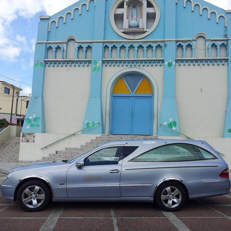 Un break argenté garé devant une église bleue avec une porte cintrée et des marches.