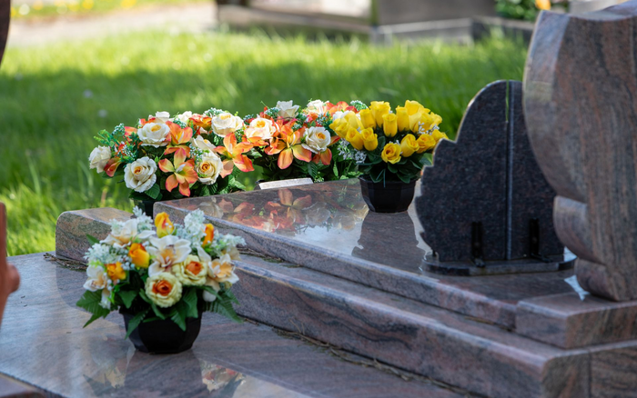 Compositions florales sur une pierre tombale de cimetière, avec des fleurs jaunes, orange et blanches.