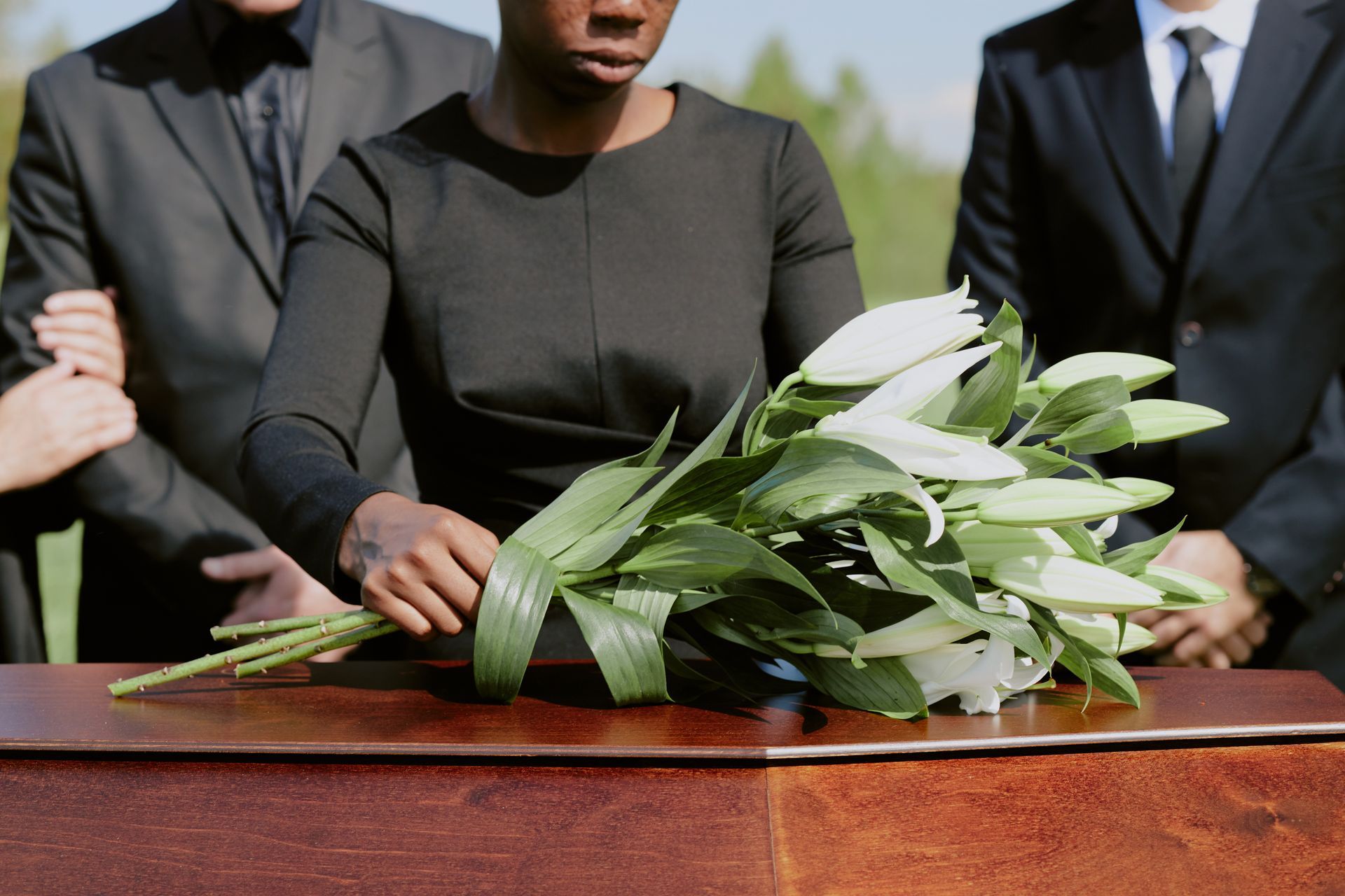 Des personnes en deuil se tiennent près d'un cercueil orné d'une composition de fleurs blanches lors d'une cérémonie d'inhumation.