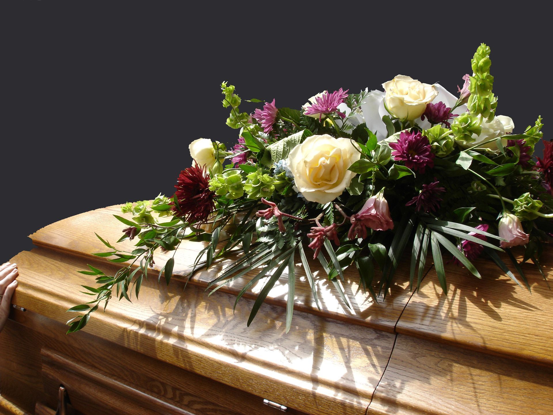 Cercueil en bois orné d'un bouquet de fleurs blanches, roses et bordeaux.