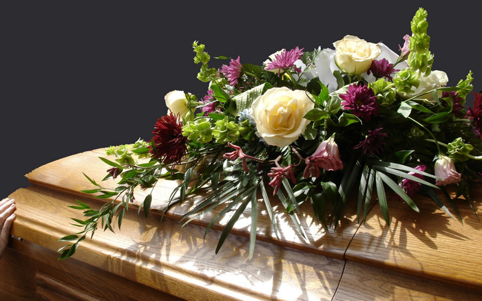 Cercueil recouvert de fleurs blanches, roses et violettes et de verdure.