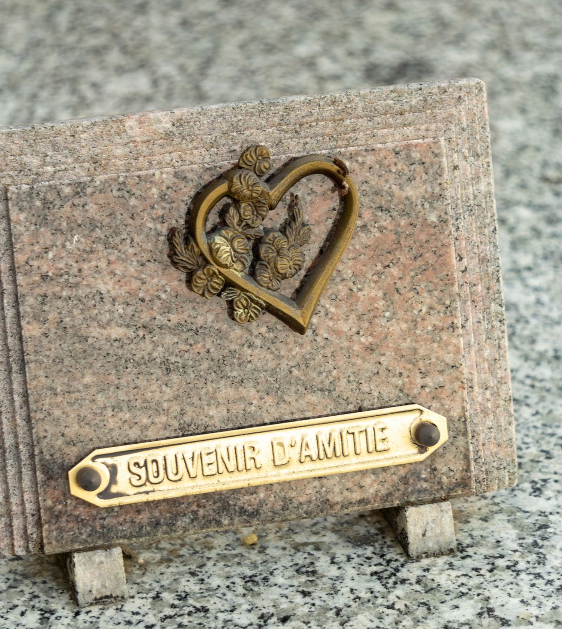 Petite plaque souvenir avec un emblème en forme de cœur et une inscription dorée sur une surface en granit.