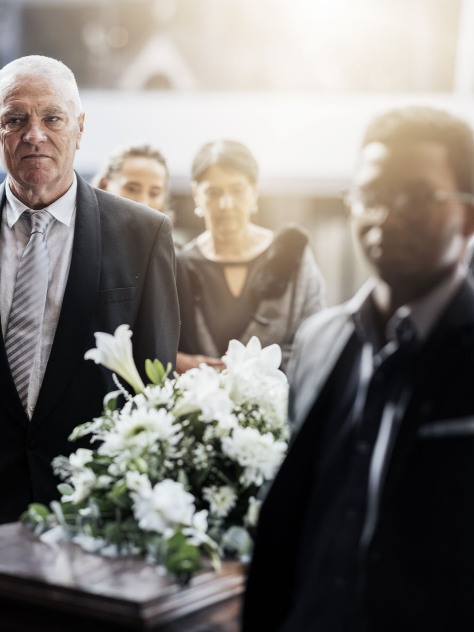 Lors d'une cérémonie funéraire en intérieur, les personnes en deuil portent un cercueil orné de fleurs.