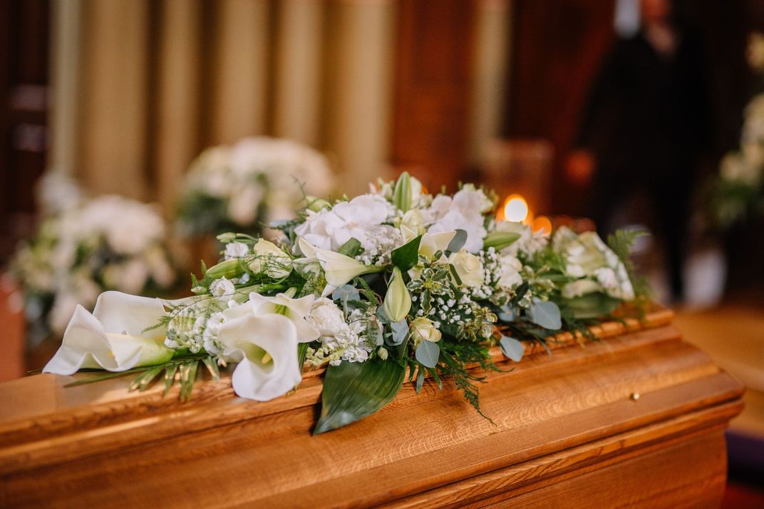 Un bouquet de fleurs blanches et vertes orne un cercueil en bois dans une église.