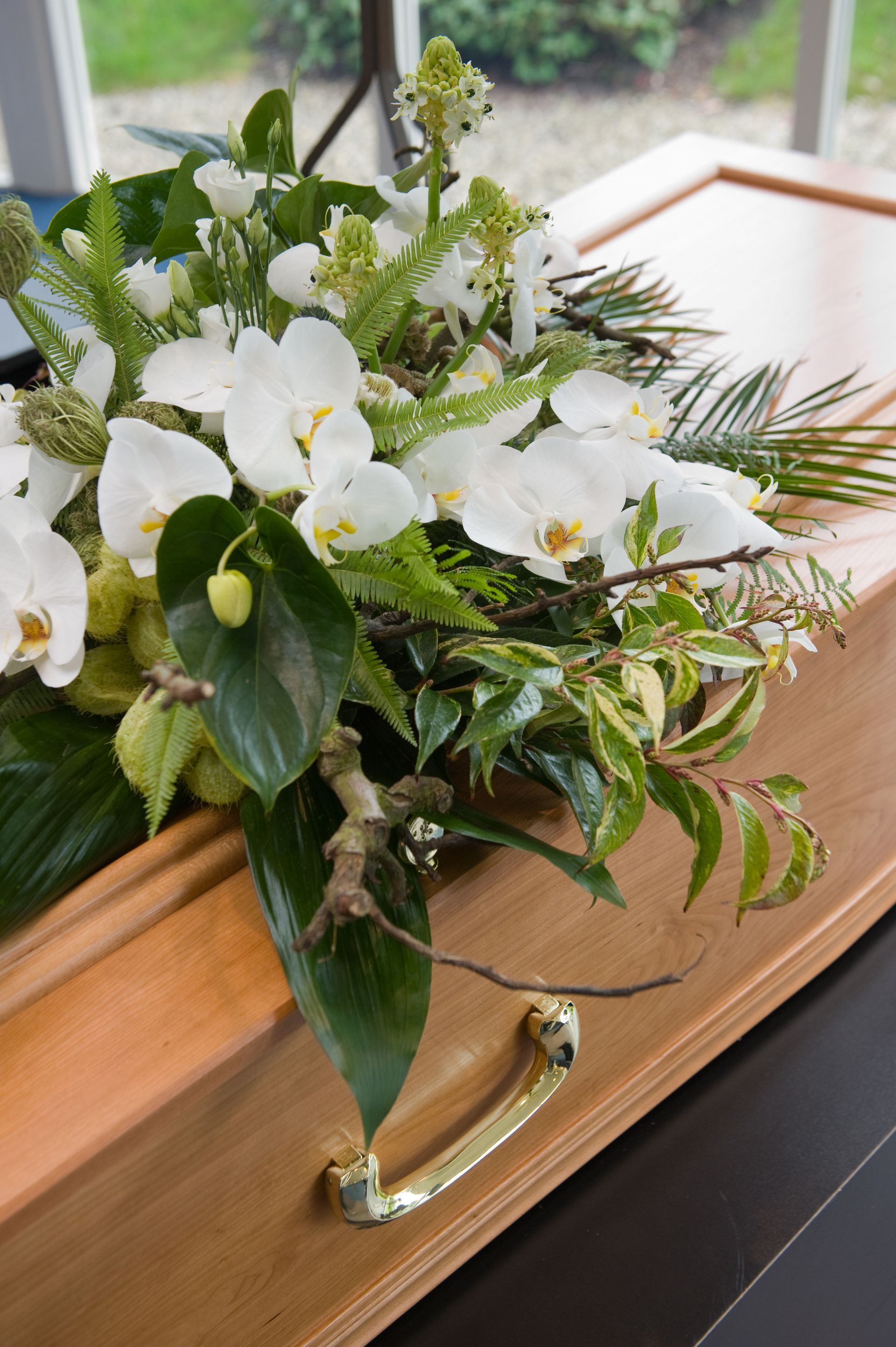 Composition florale blanche avec des feuilles vertes posée sur un cercueil en bois.
